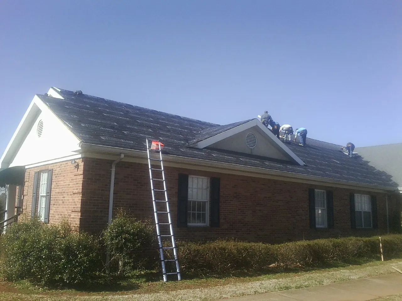 Crew tearing shingles off a brick ranch roof with a ladder set — Emergency Roof Repair work by our crew in Rhinebeck