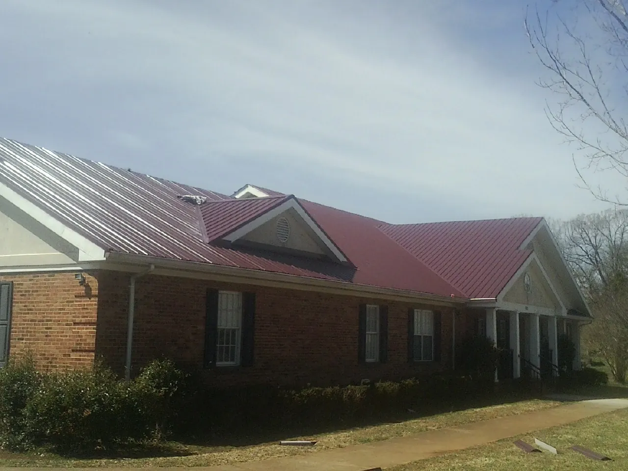 Red metal roof with gabled entries on a long brick building, from a Hail Damage Roof Repair job in Rhinebeck