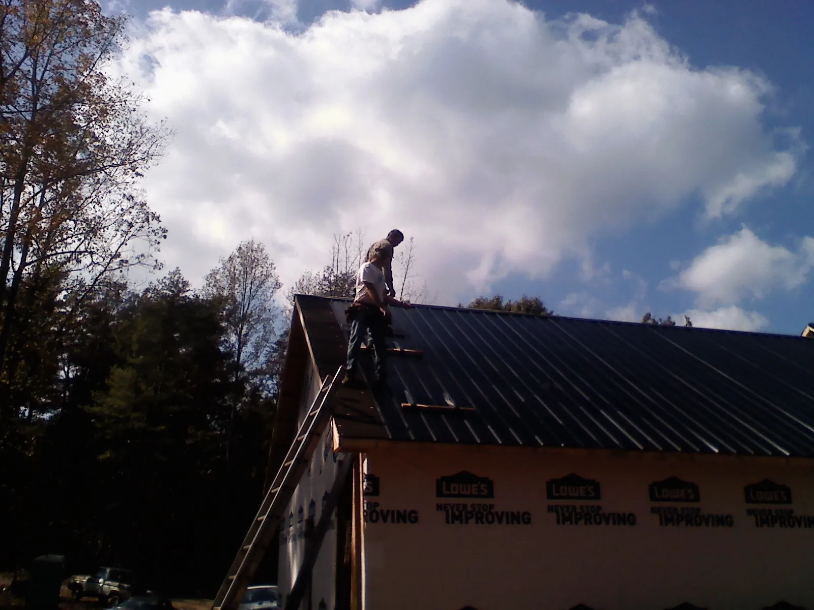 Roofer fastening dark metal panels high against a cloudy sky, from a Roof Inspection job in Rhinebeck