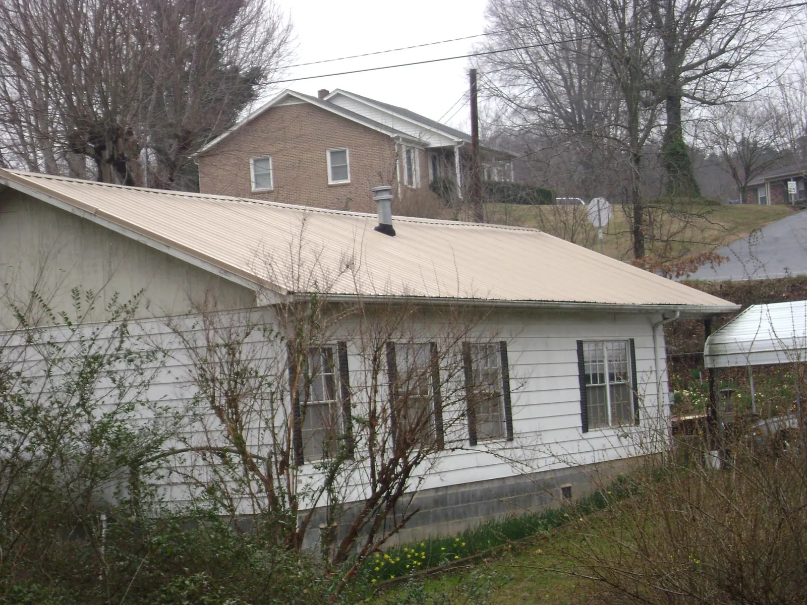 Tan metal roof on a white sided house set into a hillside — Commercial Roofing by Roofing Brothers in Rhinebeck